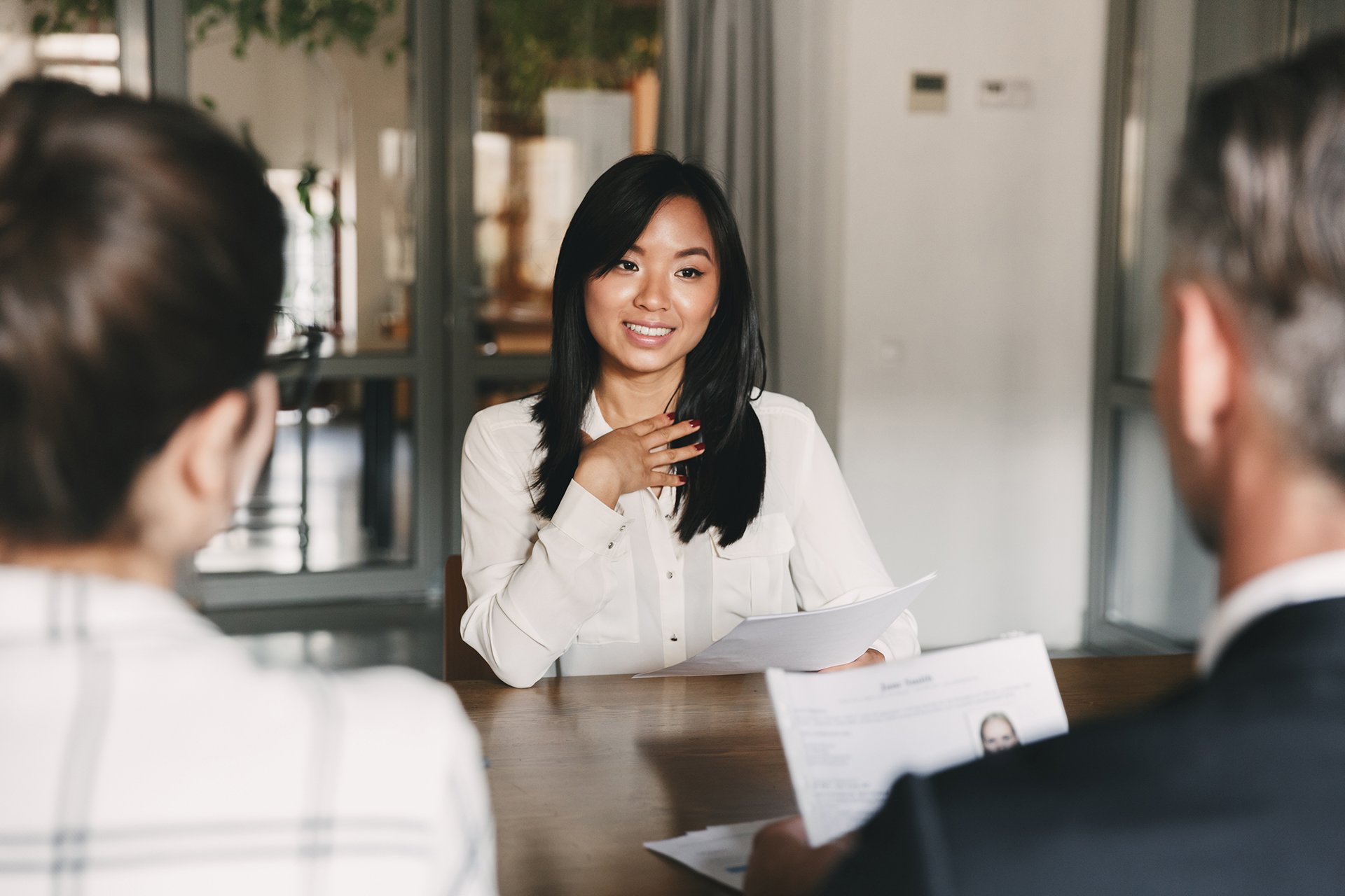 Business, career and placement concept - young asian woman smiling and holding resume while sitting in front of mentor or managers during job interview