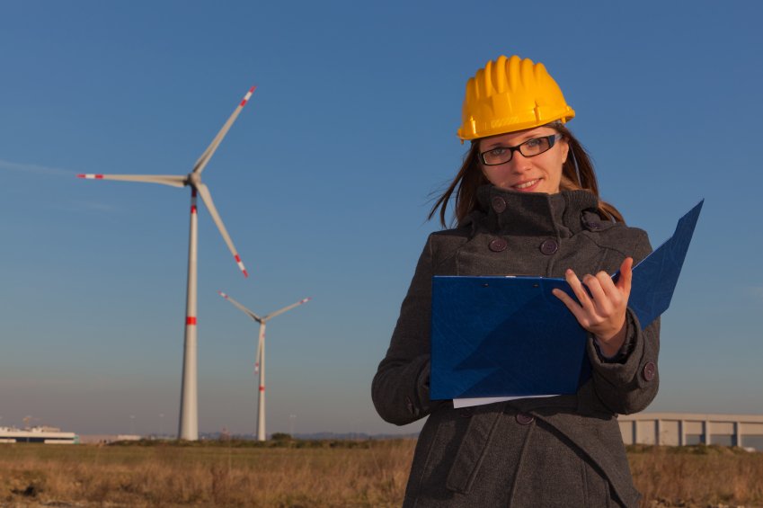Woman with a hardhat on writing in a notebook at a wind farm